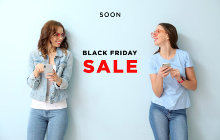 Young women with mobile phones on color background. Black Friday saleの写真素材