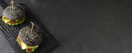 Tasty burgers with black bun on dark background with place for textの写真素材