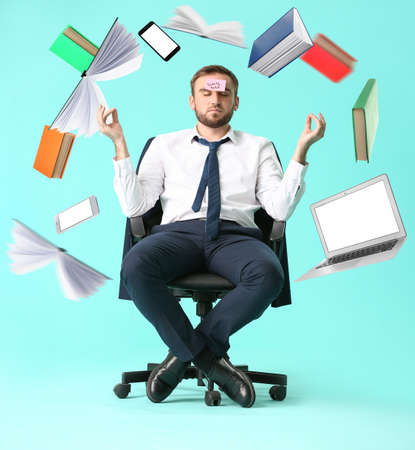 Flying objects and meditating young businessman sitting on chair against color background. Zen...