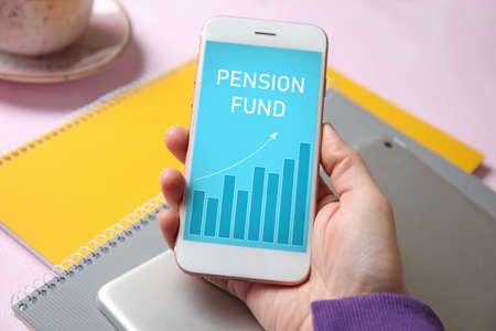 Woman holding mobile phone with open page of online pension fund on tableの写真素材