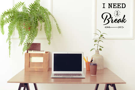Stylish workplace with modern laptop and cup of coffee near white wall with text I NEED A BREAK