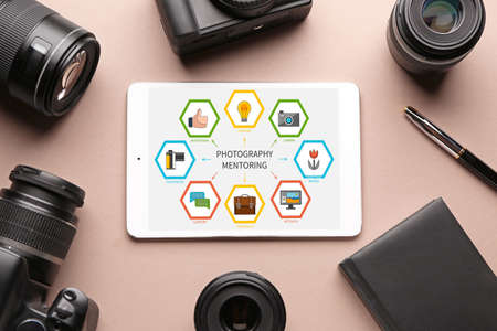 Tablet computer with interface of mentoring program on screen and set of photographer's equipment on...