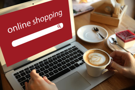 Young woman with cup of coffee using laptop for online shopping in cafeの写真素材