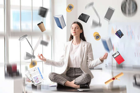 Different things flying around young businesswoman meditating in office. Zen conceptの写真素材