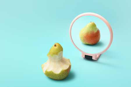 Bitten pear looking at its reflection in mirror on color backgroundの写真素材