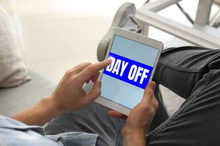 Young man with tablet computer dreaming about vacation at home