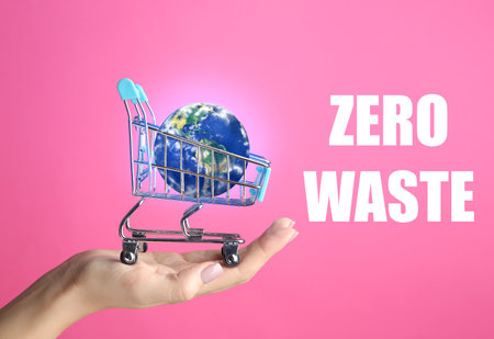 Female hand with small planet Earth in shopping cart on color background. Zero waste conceptの写真素材