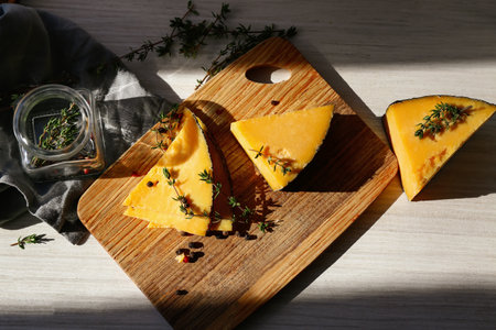 Wooden board with tasty cheese, thyme and spices on white tableの写真素材