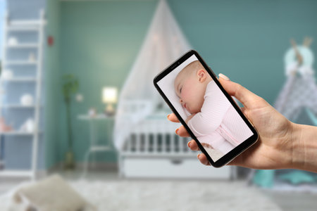 Mother using modern mobile phone as baby monitor at homeの写真素材