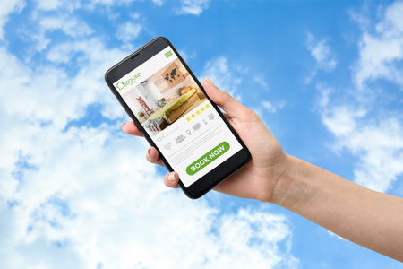Female hand with mobile phone against blue sky. Concept of booking room in hotel onlineの写真素材