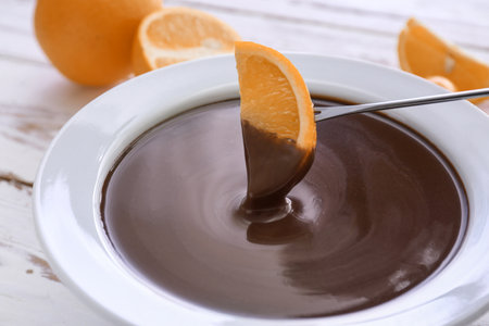 Dipping of tasty orange into bowl with chocolate fondue on tableの写真素材