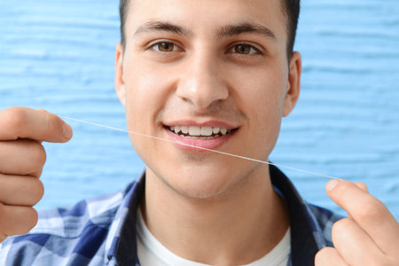 Handsome man with dental floss on color backgroundの写真素材