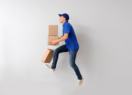 Jumping young male courier with boxes on light backgroundの写真素材