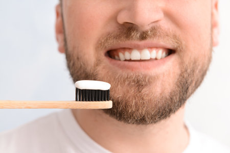 Handsome man with toothbrush and paste on light background, closeup