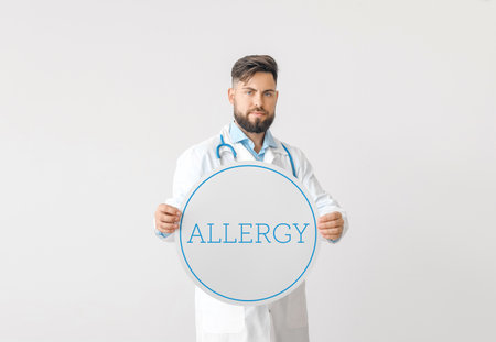 Portrait of male doctor holding poster with text ALLERGY on light backgroundの写真素材