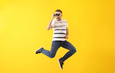 Jumping young man with photo camera on color backgroundの写真素材