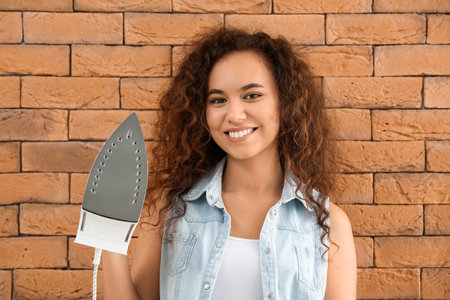 Young woman with iron on brick backgroundの写真素材