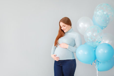 Beautiful pregnant woman with balloons on light backgroundの写真素材