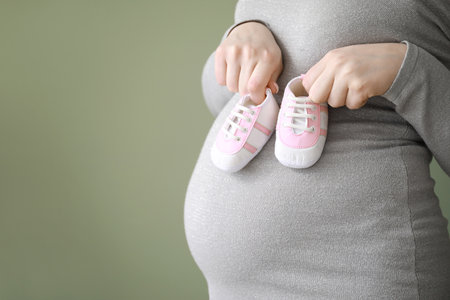 Beautiful pregnant woman with baby booties on color background, closeupの写真素材