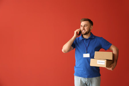 Handsome delivery man talking by phone on color backgroundの写真素材