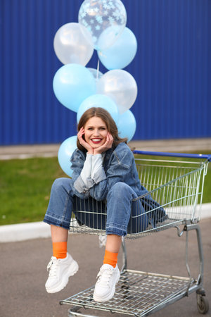 Young woman with balloons sitting in shopping cart outdoorsの写真素材