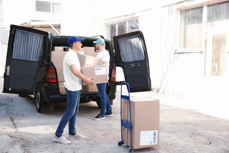 Delivery men taking parcels from car outdoors