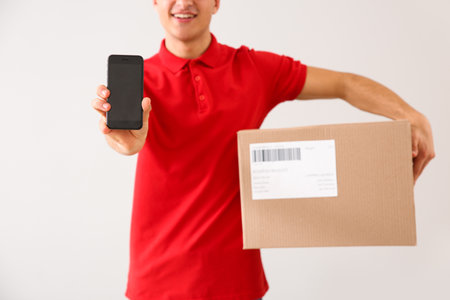 Delivery man with box and mobile phone on light backgroundの写真素材