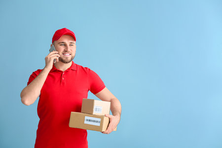 Handsome delivery man with boxes talking by phone on color backgroundの写真素材