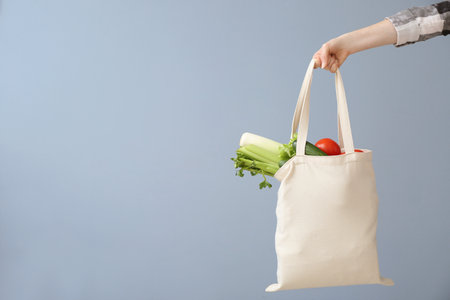 Female hand with eco bag on gray background. Zero waste concept