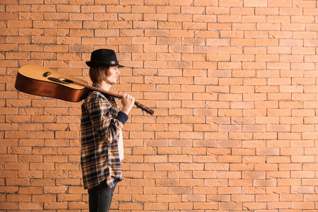 Handsome young man with guitar near brick wallの写真素材