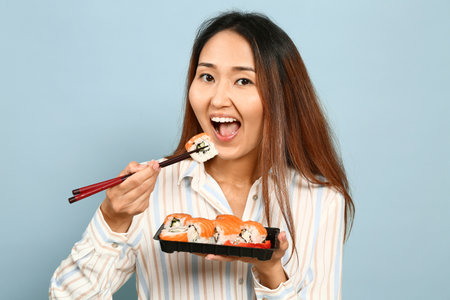 Asian woman eating sushi on color backgroundの写真素材