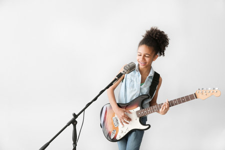 African-American girl playing guitar and singing against light backgroundの写真素材