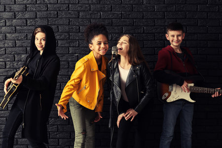 Band of teenage musicians playing against dark wall