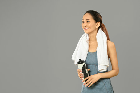 Sporty Asian woman with bottle of water on gray backgroundの写真素材