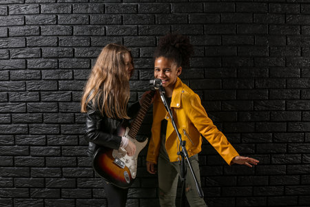 Teenage girls playing guitar and singing against dark wallの写真素材