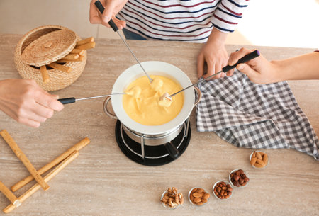 Women eating tasty cheese fondue at tableの写真素材