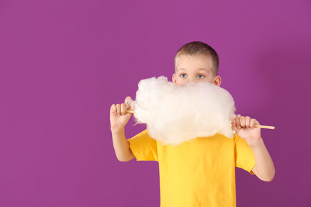 Cute little boy with cotton candy on color backgroundの写真素材