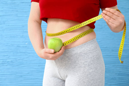 Overweight woman with apple and measuring tape on color background. Weight loss concept