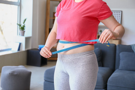 Overweight woman with measuring tape at home. Weight loss conceptの写真素材