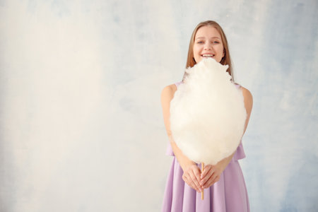 Beautiful woman with cotton candy on light backgroundの写真素材