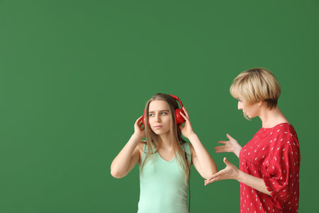 Mother talking to daughter who is listening to music on color backgroundの写真素材