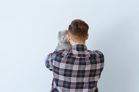 Young man with cute funny cat on light backgroundの写真素材