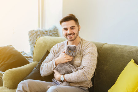 Young man with cute funny cat at homeの写真素材
