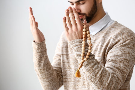 Young Muslim man praying against light backgroundの写真素材