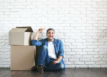 Handsome mature man with moving boxes near white brick wall