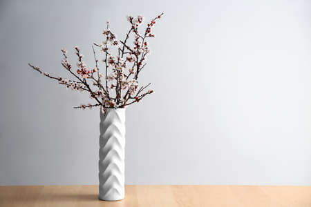 Vase with beautiful blossoming branches on table against light backgroundの写真素材