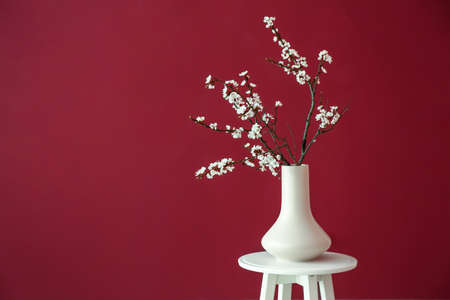 Vase with beautiful blossoming branches on table against color background