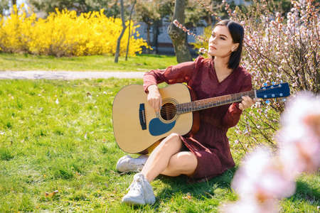 Beautiful young woman playing guitar in park on spring day