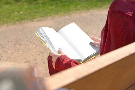 Beautiful young woman reading book on bench in park, closeup