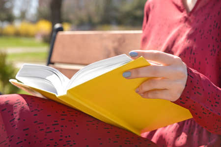 Beautiful young woman reading book on bench in park, closeupの写真素材